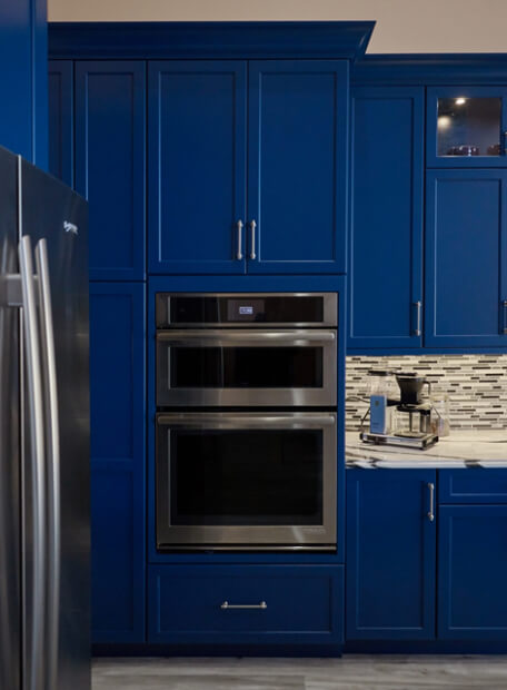A dark and vibrant blue kitchen with custom painted cabinets showing an inset wall oven appliance.