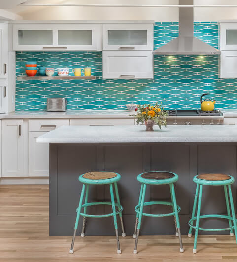 A bright and vibrant kitchen design with a dark gray kitchen island that creates contrast tothe white cabinets and bright blue backspalsh.