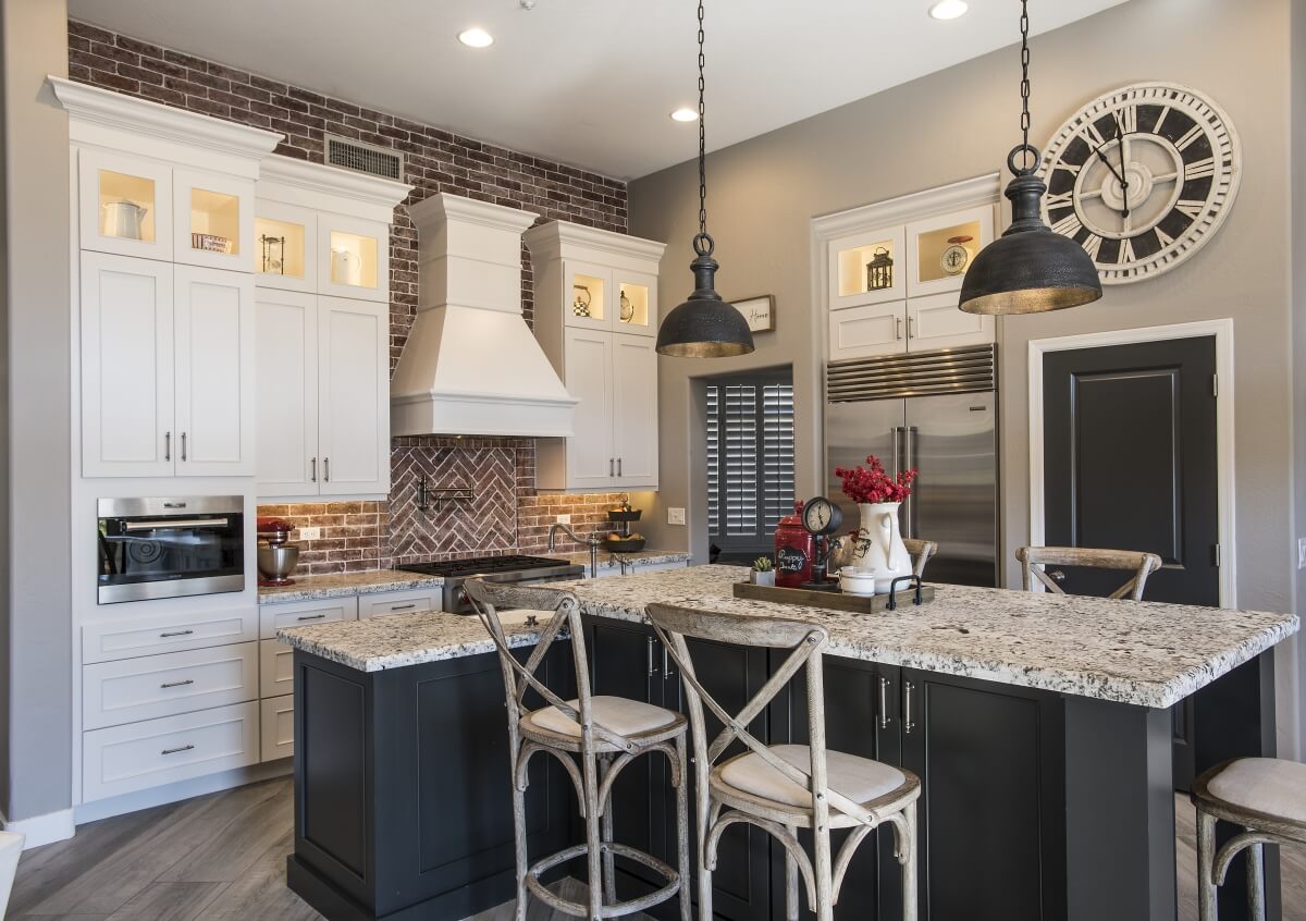 A traditional styled farmhouse kitchen remodel featuring a natural brick backsplash, a painted wood hood and a dark gray (almost black) kitchen island.