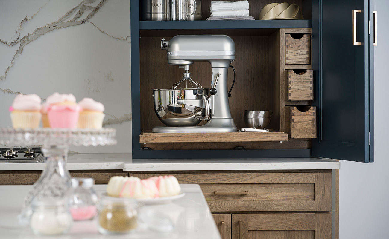 An organized kitchen cabinet with functional storage for a hidden beautiful baking center. A roll-out shelf holds a powered mixer.