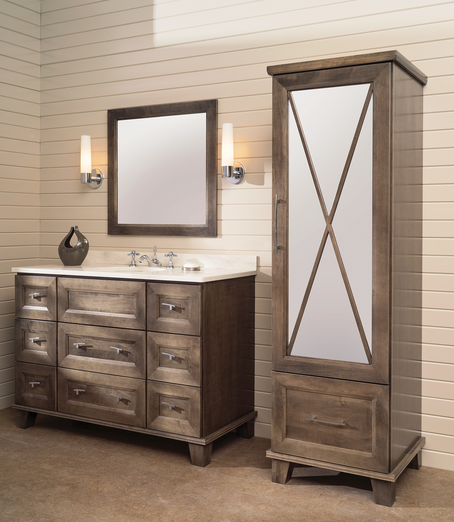 A gray stained bathroom vanity and a tall furniture linen cabinet with an X patterned mullion on a mirrored cabinet door.
