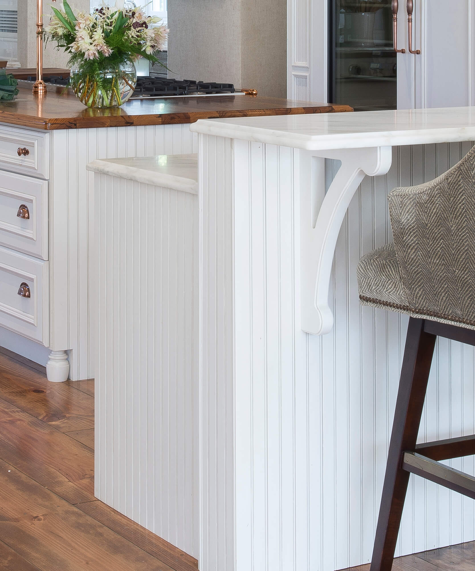 A white painted kitchen peninsula with two countertop levels to create a clean-up workspace on one side and a breakfast bar space on the other.