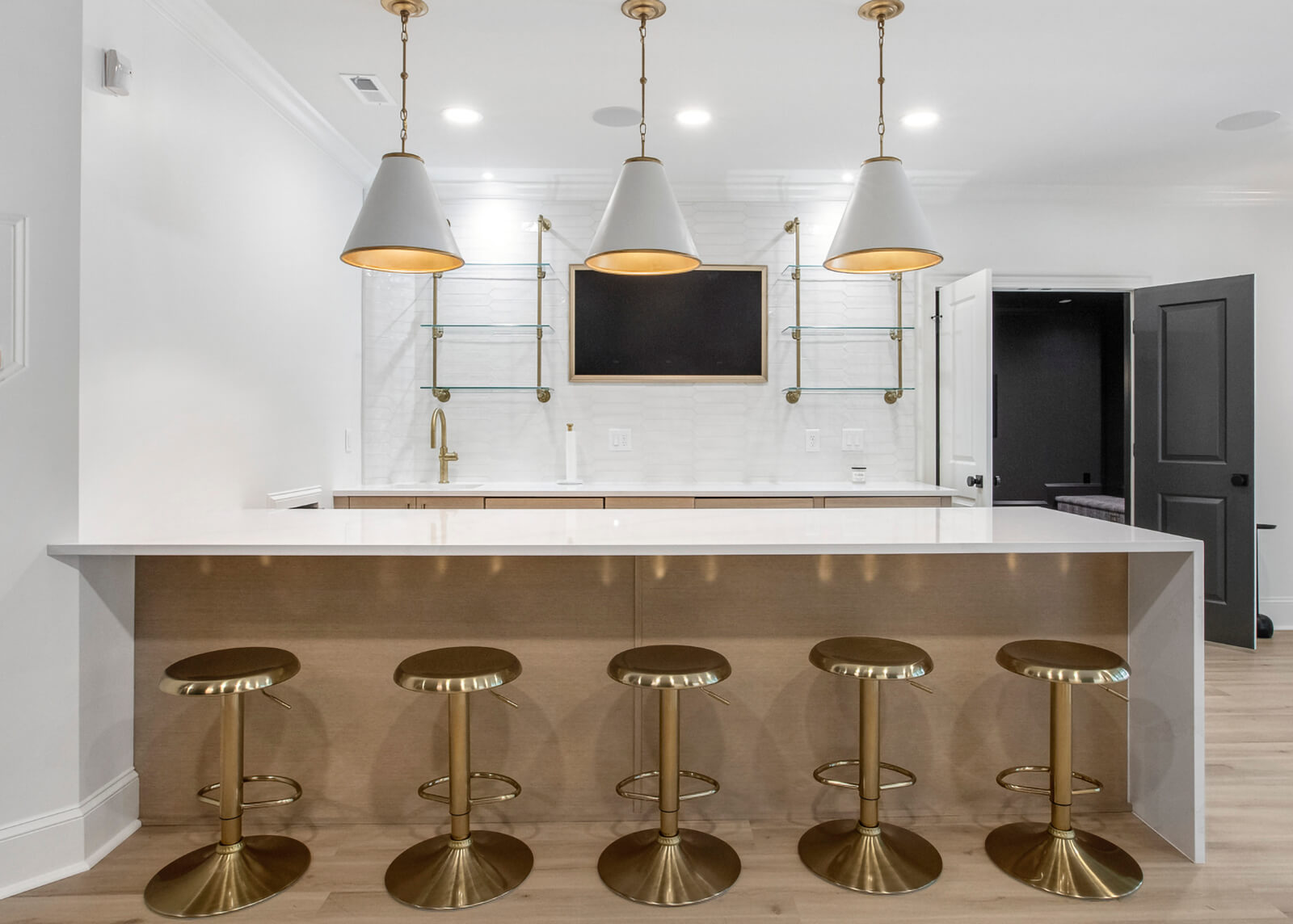 A white and gold luxury home bar features a modern styled kitchen peninsula with lost of bar stool seating and a waterfall countertop.