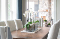 A coastal inspired modern farmhouse dining room with a long chandelier and wood table.