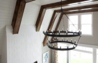 A close up unique vaulted ceilings with large beams and shiplap detail with a large black chandelier light fixture.