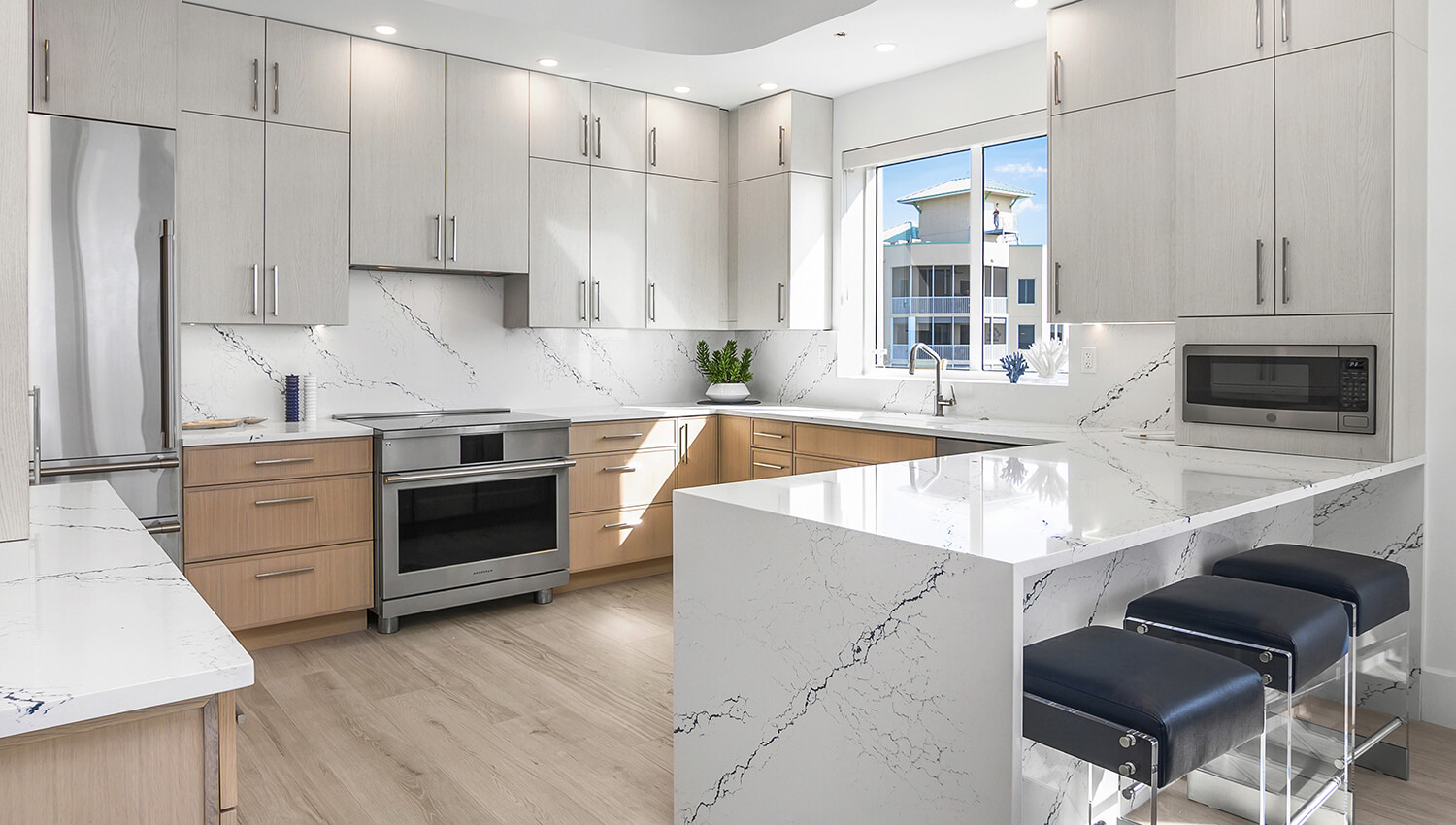 A contemporary beach house kitchen with two-toned slab cabinet doors and a quartz kitchen peninsula with a waterfall countertop and stool seating for three.