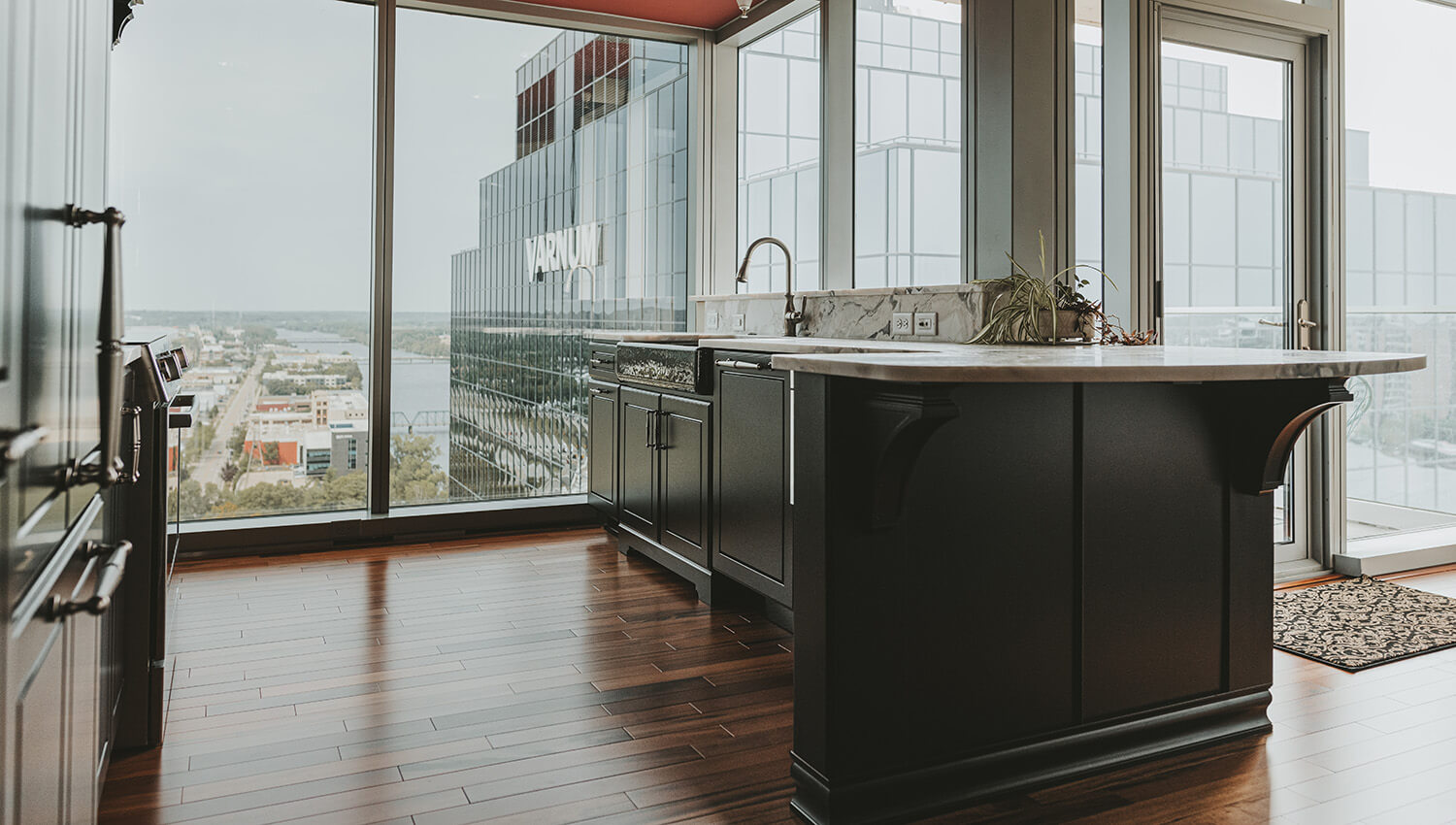 A kitchen peninsula attached to wall in an urban apartment with floor to ceiling windows with skyline views of the city. The end of the peninsulat cabinet as a curved counter for comfortable bar stool seating.