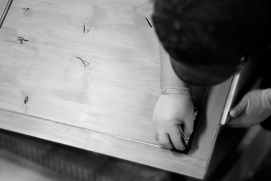 A professional cabinet maker wiping the stain application on a kitchen cabinet door to create a luxurious finish.