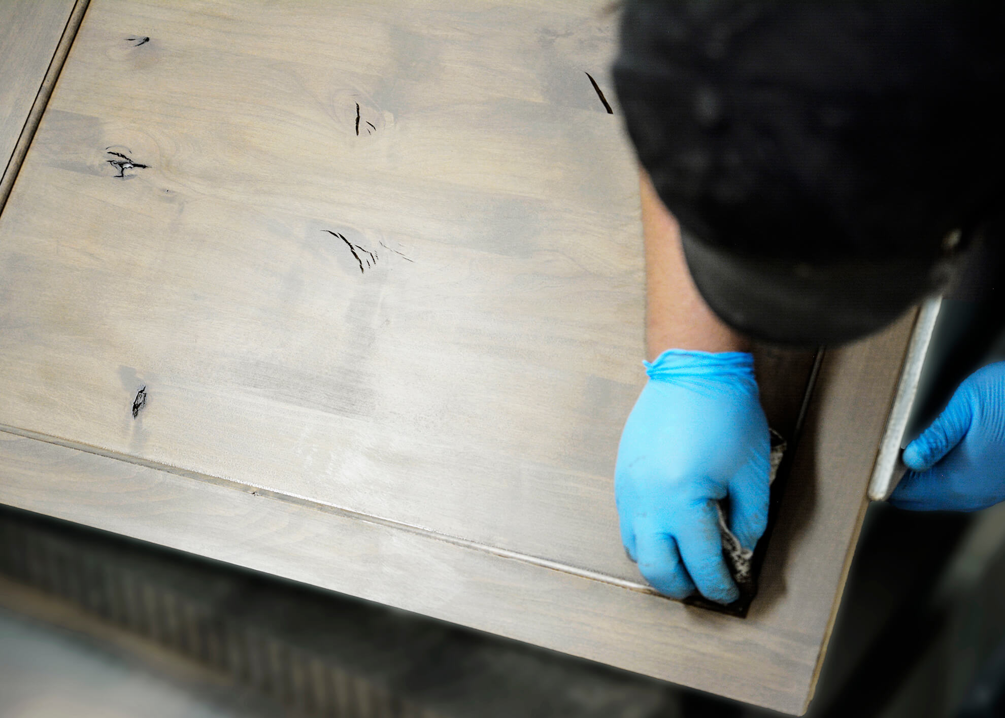 Close up of a cabinet maker and finish artisan hand wiping a stain and glaze finish on a wood cabinet door. Made in America cabinetry.