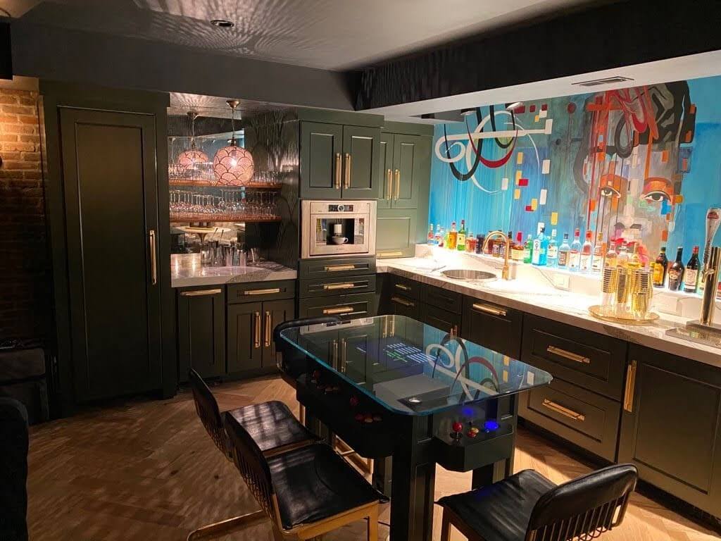 A home bar basement remodel with dark green cabinets and a mirror backsplash to bounce the decorative light patterns of the Moroccan pendant lights.