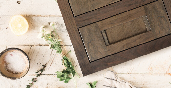 A beautiful inset cabinet door style shown in a medium, true-brown stain color on cherry wood is shown in a flat lay format over some off-white painted wood planks.