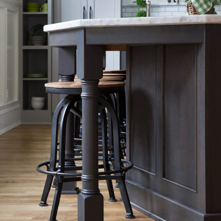 A close up of a gray stained kitchen island and turned post with stool seating.