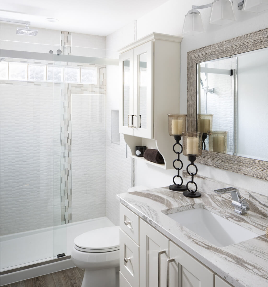 The small cabinet above the toilet in this bathroom uses mirror to help reflect more light from the small bathroom window throughout the space. Dura Supreme design by Gwen Adair of Cabinet Supreme by Adair, Wisconsin. Photography by Ryan Hainey.