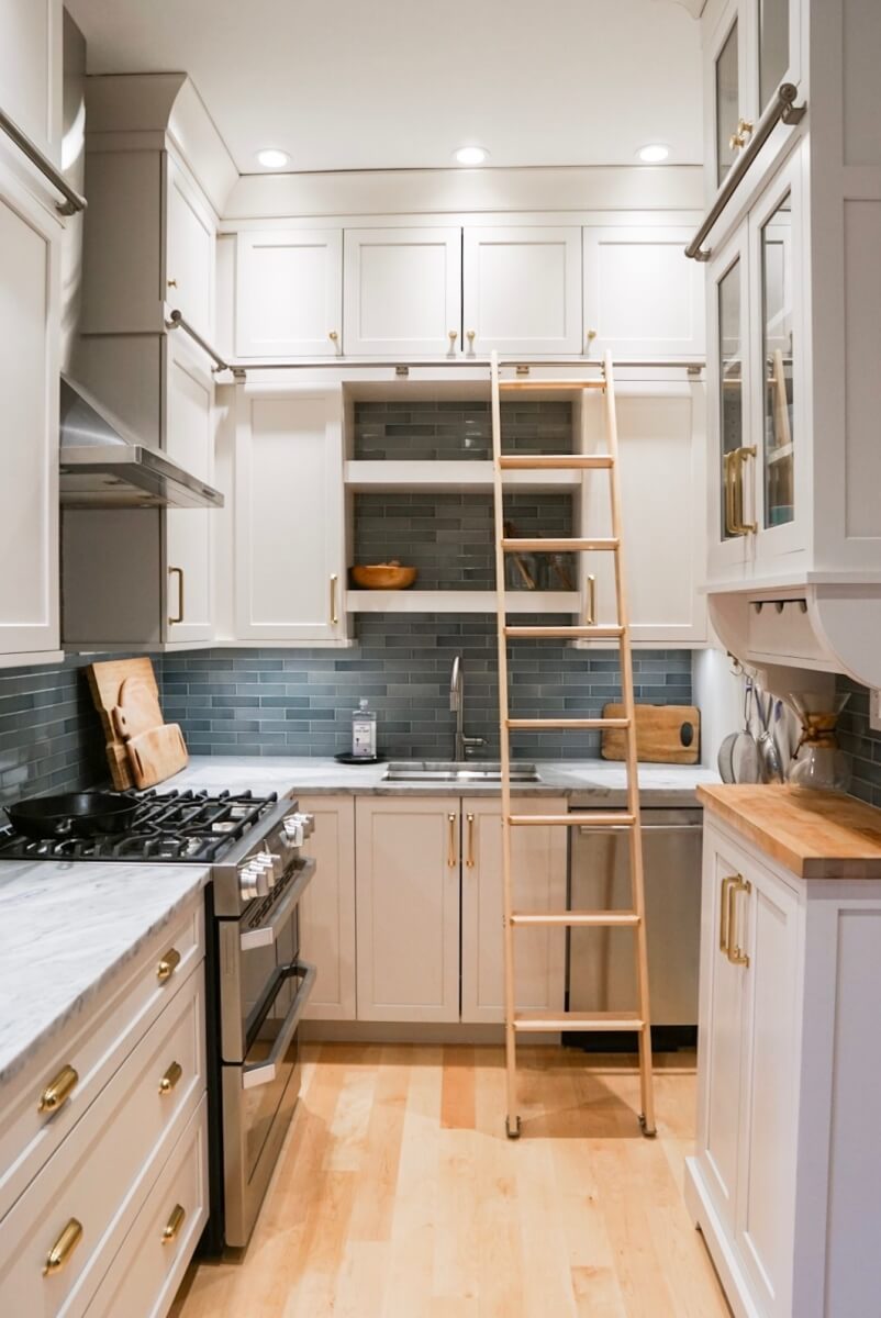 A small U-Shaped kitchen design in a historic home with white painted cabinetry and a library style ladder.