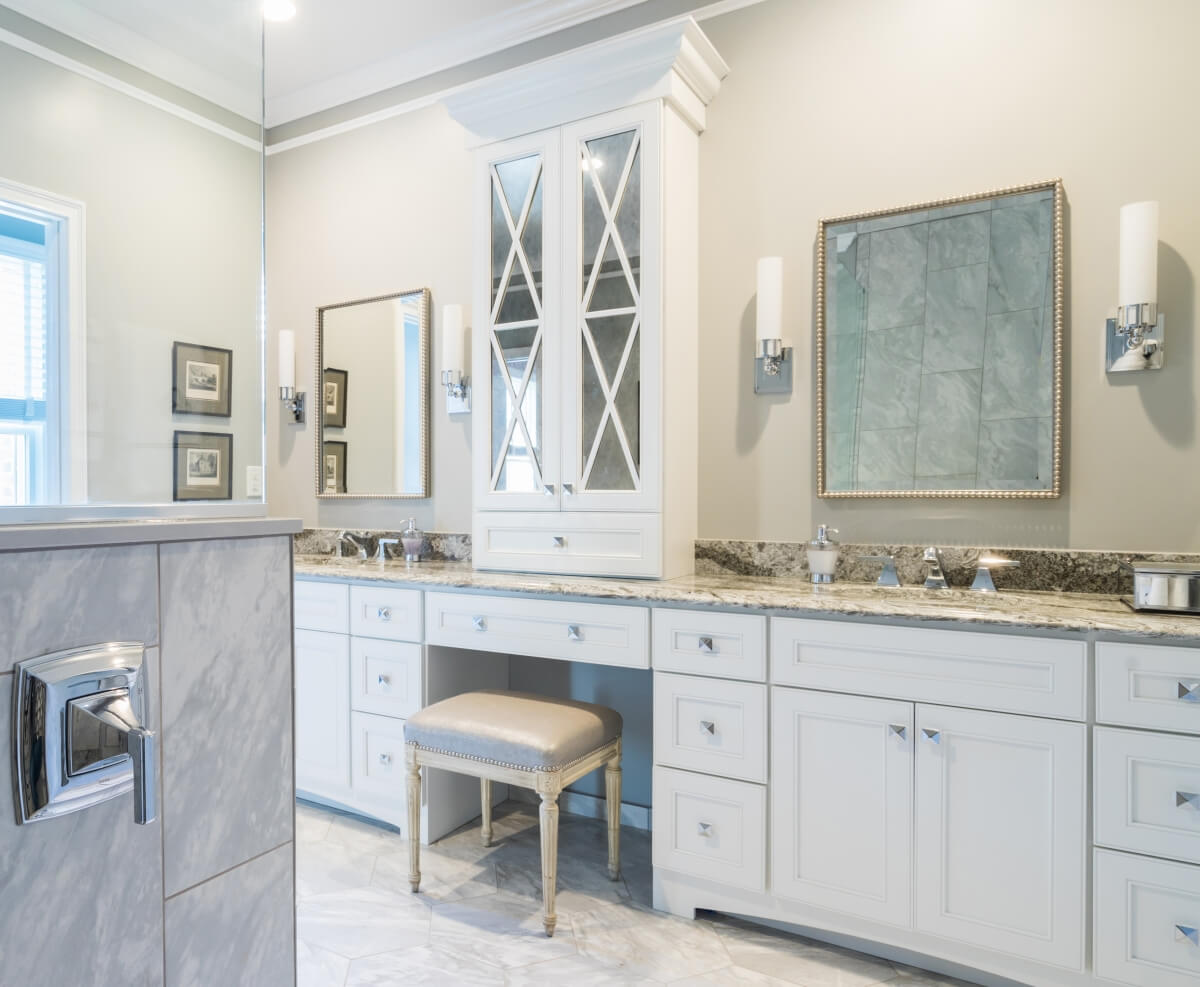 A double sink vanity with a tall tower in the center dividing the two spaces. The countertop sitting cabinets feature elegant mirrored cabinet doors and mullion designs.