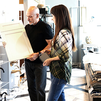 A kitchen designer working with a client in a kitchen & bath showroom. The homeowner is shopping for new kitchen cabinets and making decisions on the door style and finish colors.