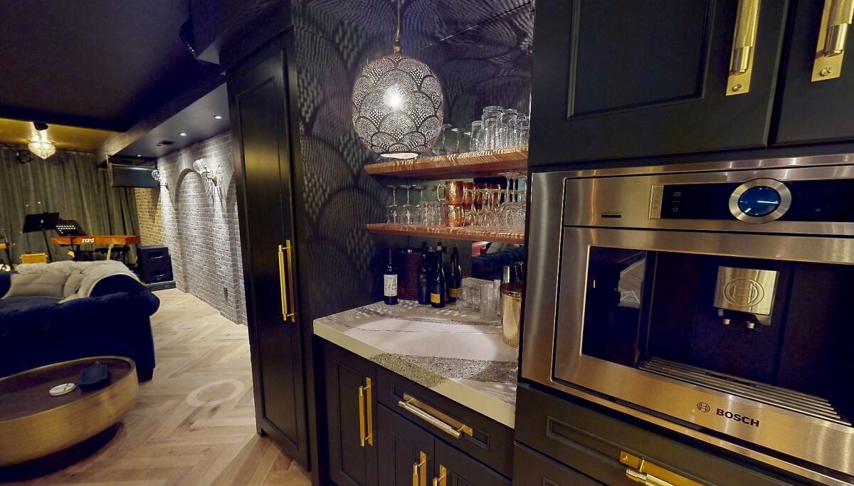 A close up of reflective lights on a mirror backsplash with dark green cabinets in a home bar. A newly remodeled basement design for entertaining.