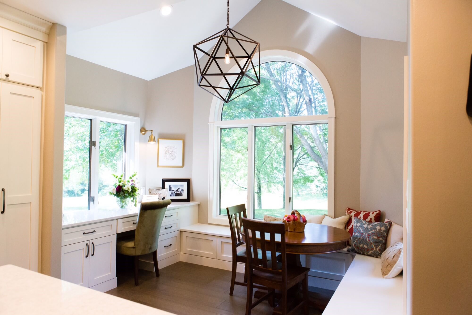 A kitchen breakfast nook and home office combination with one large scale and artisitc light fixture.