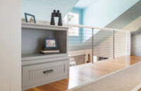 A close up of a small built-in cabinet with a cottage style and gray painted finish in a lofted hallway of a beach cottage home.