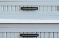 A close up of gray painted kitchen cabinet doors and drawers with a cottage bead board panel and shaker style.