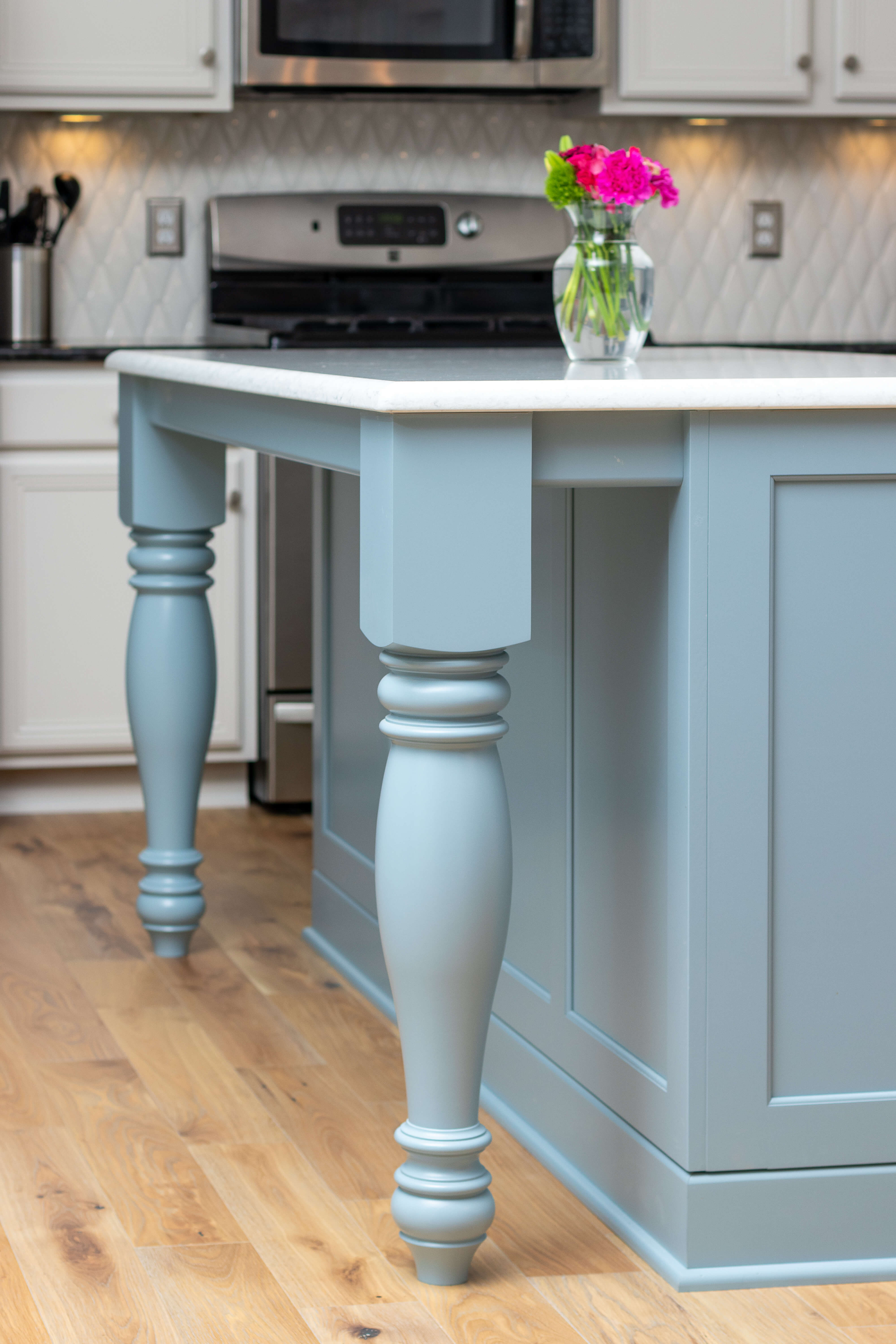 A close up of a light blue painted kitchen island with a decorative furniture style turned post.