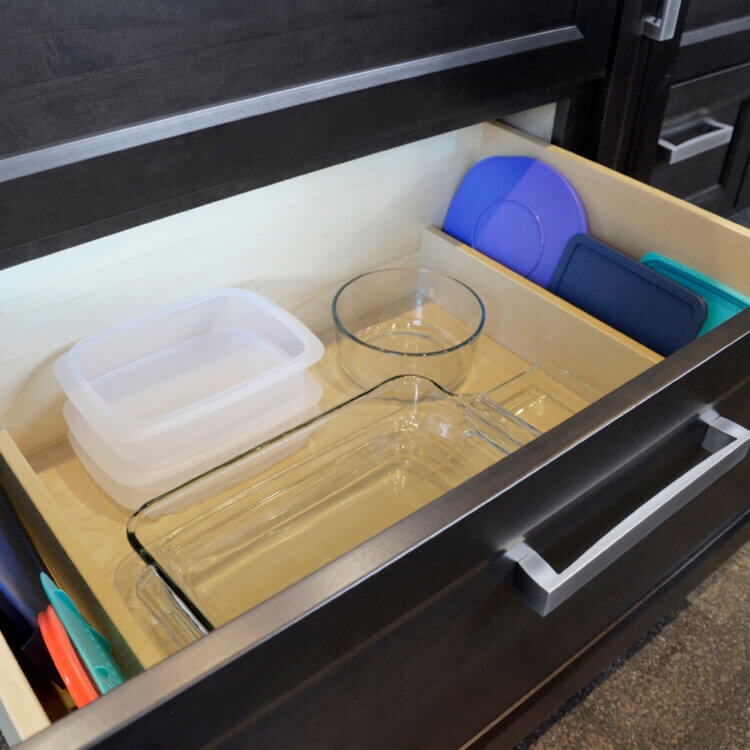 Plastic and glass containers and lids storage in a kitchen drawer. Dividers on the sides of the drawer create an organized spot for the lids.
