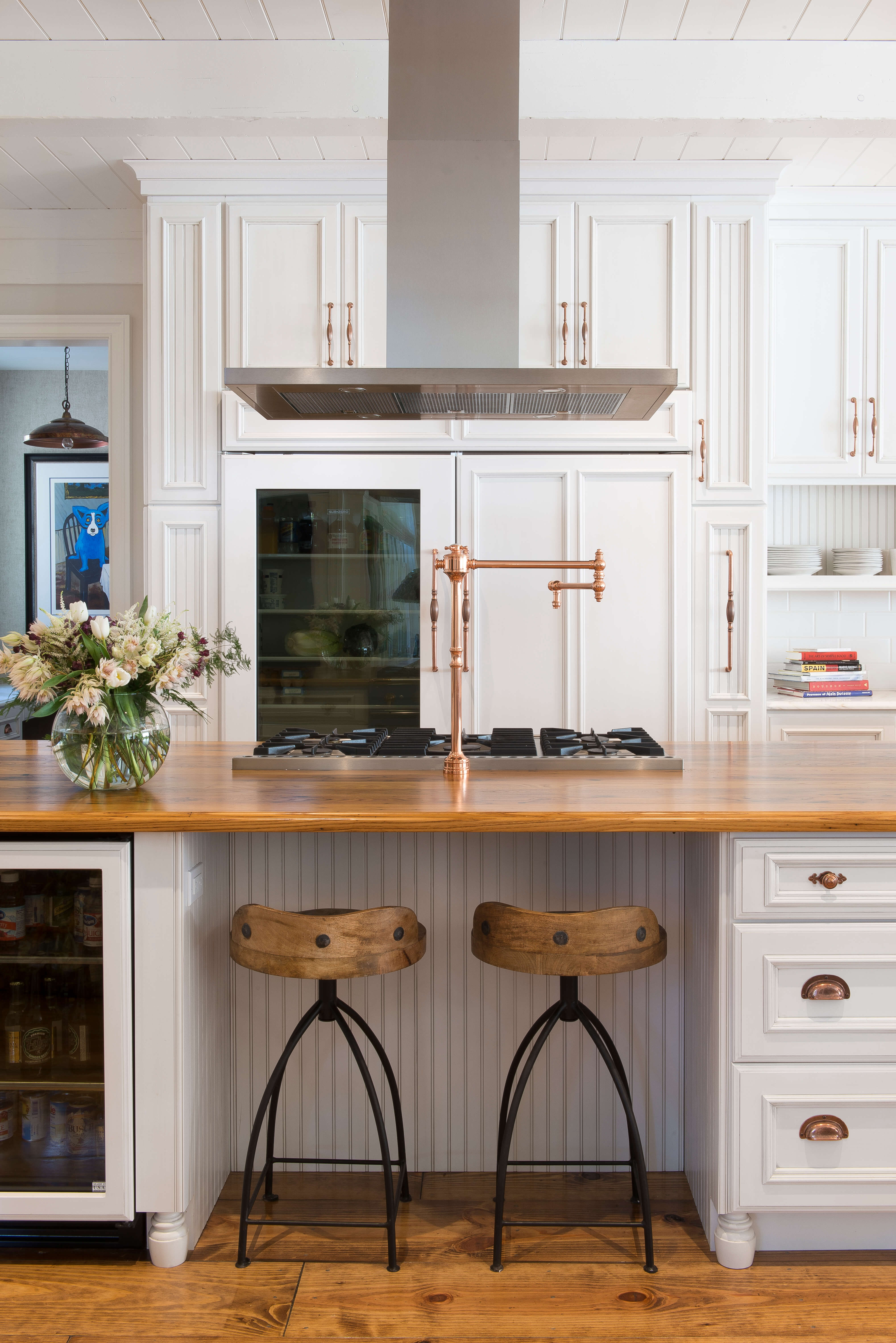 New kitchen cabinets with a white painted finish. Inset kitchen cabinets are traditional and elegant. This kitchen island has a cooktop with a wal mounted metal hood in stainless steel. There is seating for two accross from the cooktop, wood countertops, and beautiful brass hardware throughout the design.