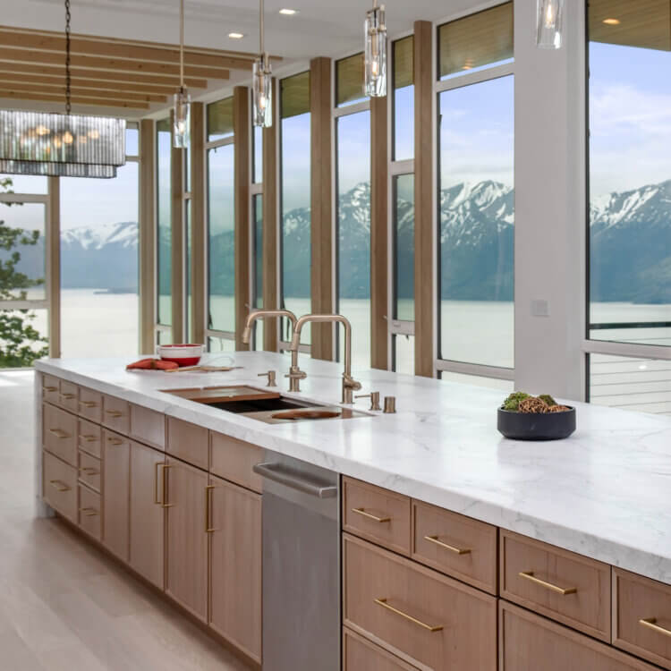 A beautiful kitchen island with a double sink and waterfall countertop with breath-taking window views of the ocean and mountains.