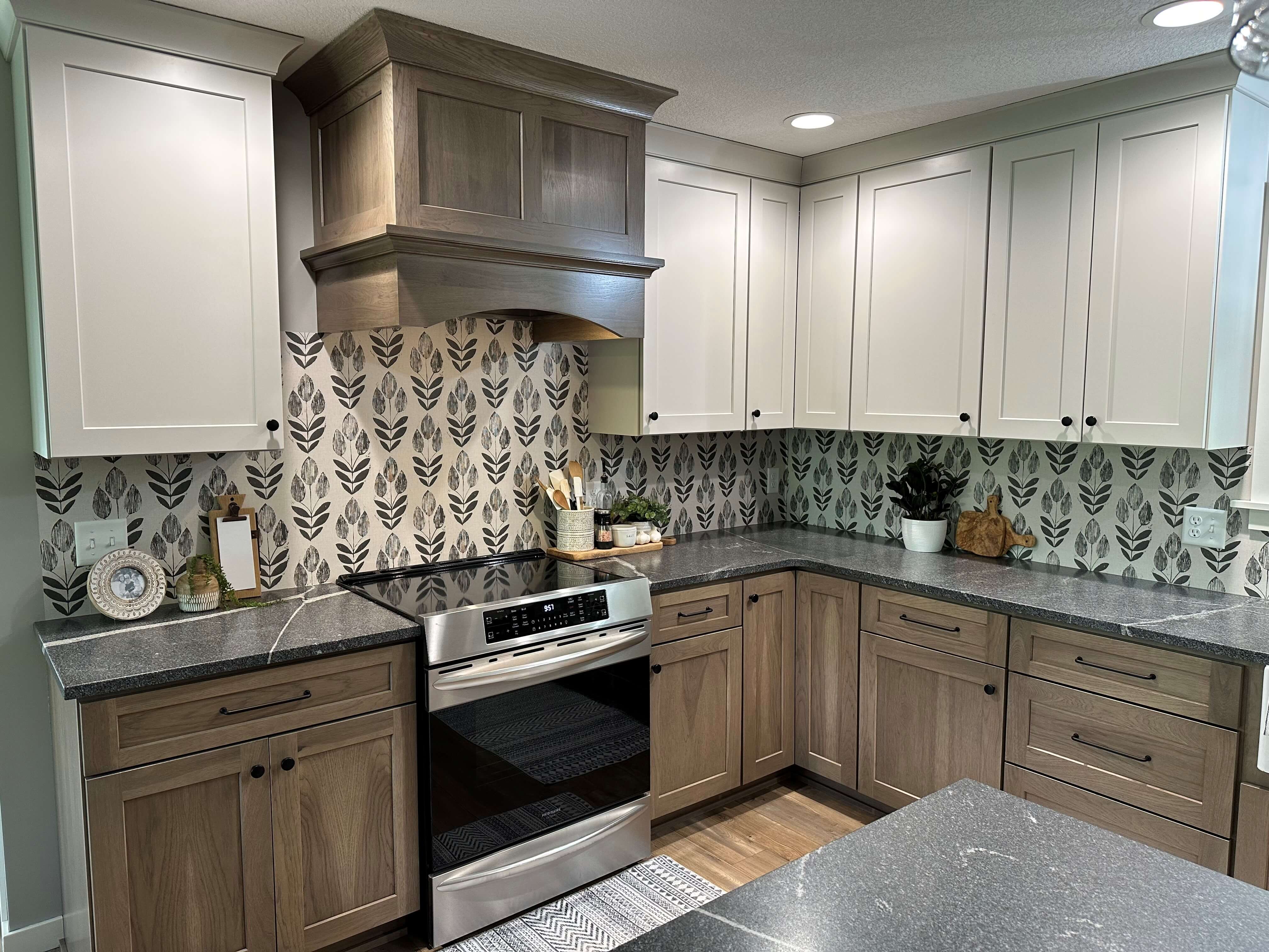 The cook zone of the kitchen features an independent wood hood that contrasts the light painted wall cabinets.