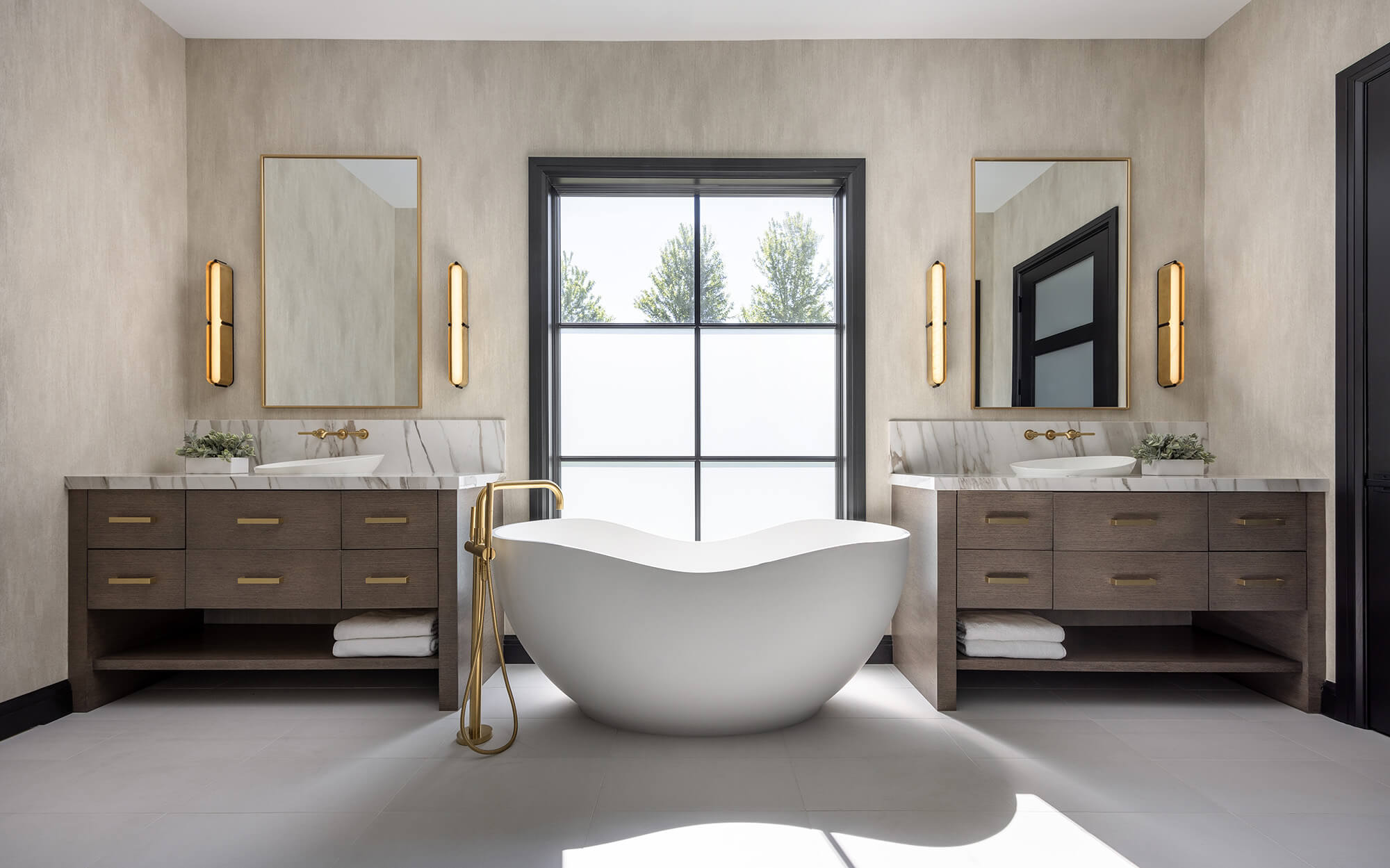 His-and-her personalized bathroom vanities feature dark true-brown stained cabinetry with a continuous horizontal grain pattern for a sleek, modern look. A freestanding soaking tub centered between the furniture-style vanities creates balance and a spa-like atmosphere.