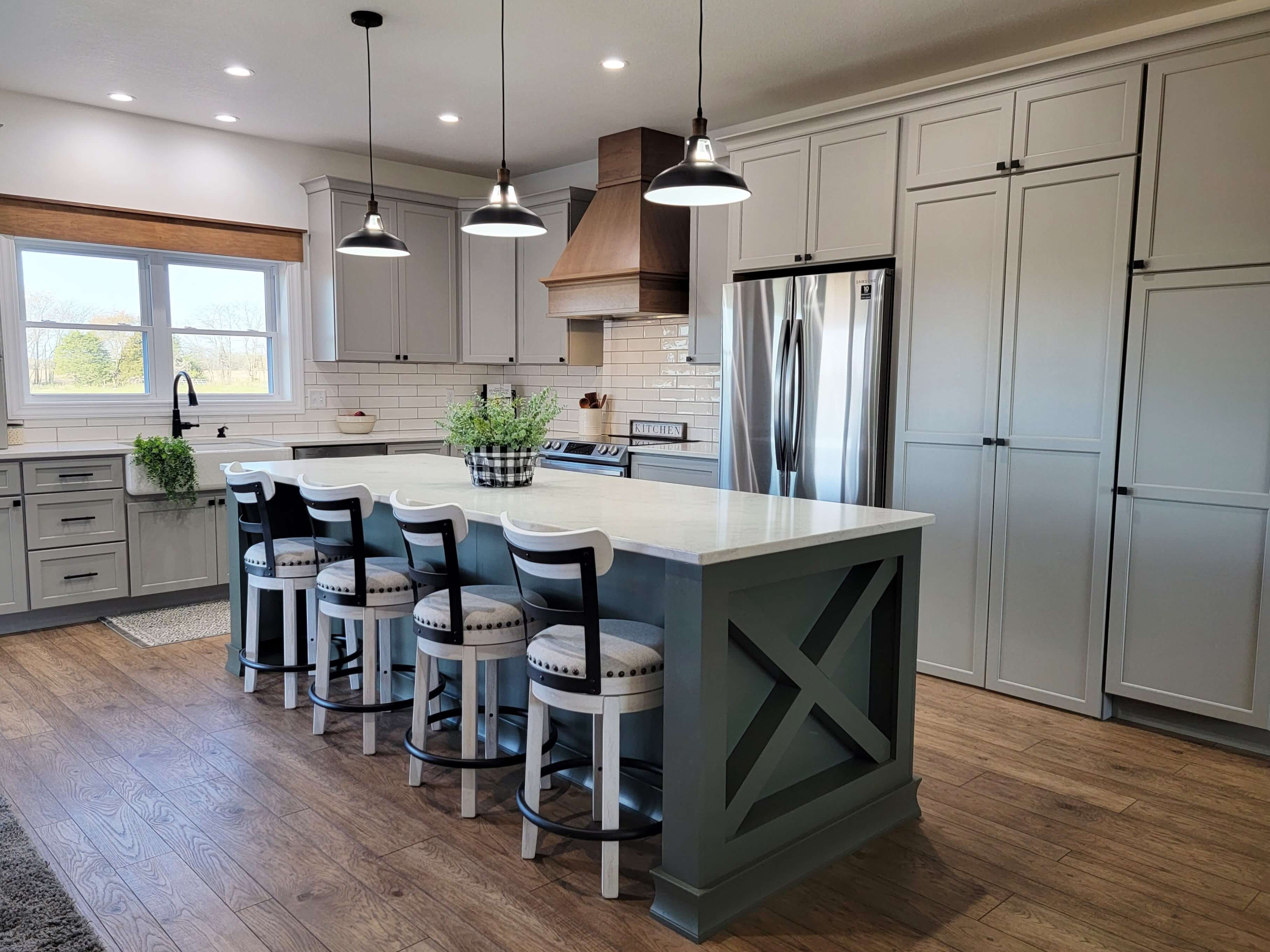 A muted off-white kitchen with a soft, natural color palette featuring an earthy green painted kitchen island with an X style end cap.