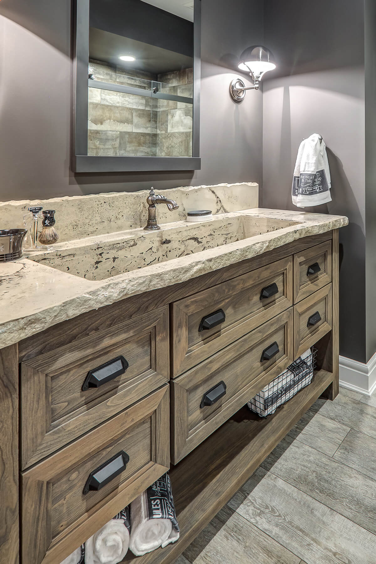 A dramatic, rustic styled bathroom with weathered wood cabinets featuring a custom furniture style with turned post legs and floor shelf below.