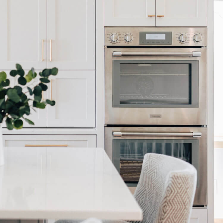 A close up of flush inset appliances in an all white kitchen design.