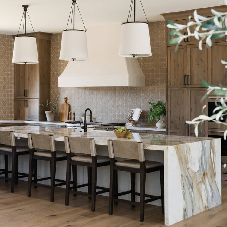 A stunning Mediterranean styled kitchen design with warm, true-brown stained cabinets with a shaker door style and a long kitchen island with a waterfall style countertop.