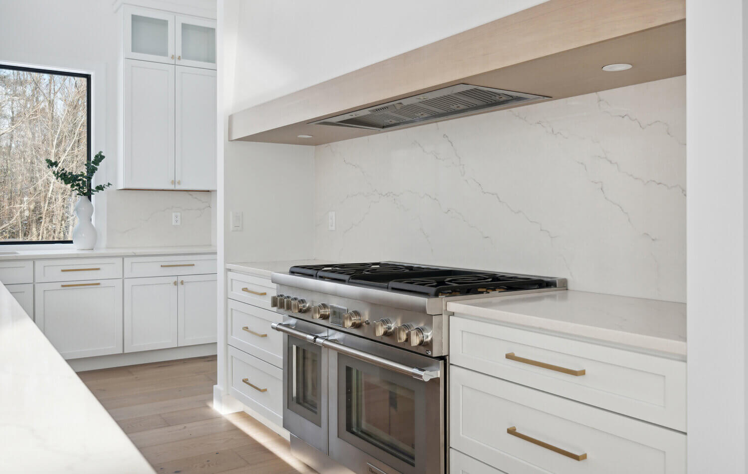 A trendy range alcove design with white cabinets and a light wood frieze accent on the wood hood.