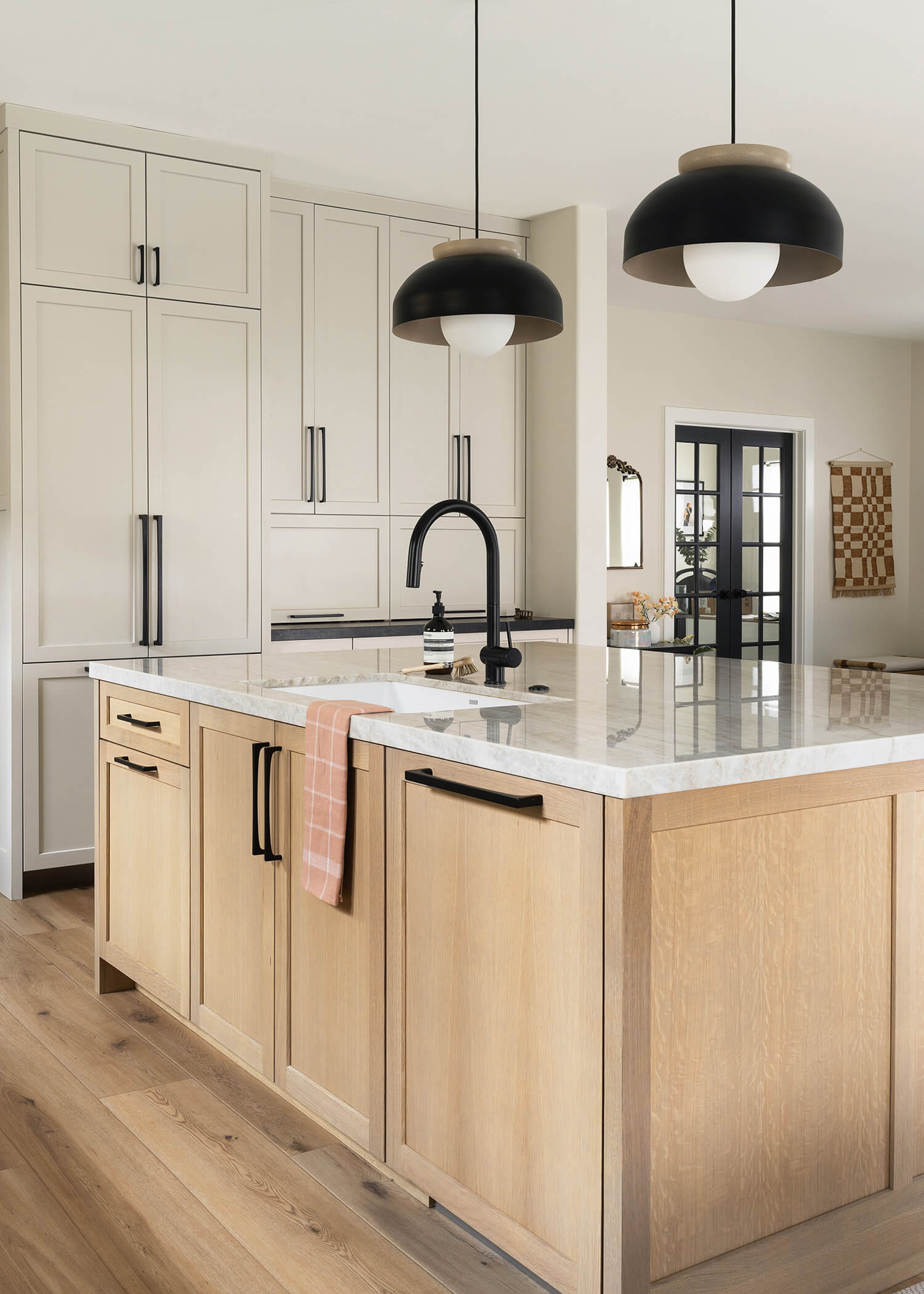 A white painted kitchen with a beautiful light stained rift sawn oak kitchen island with paneled appliances and kitchen sink.