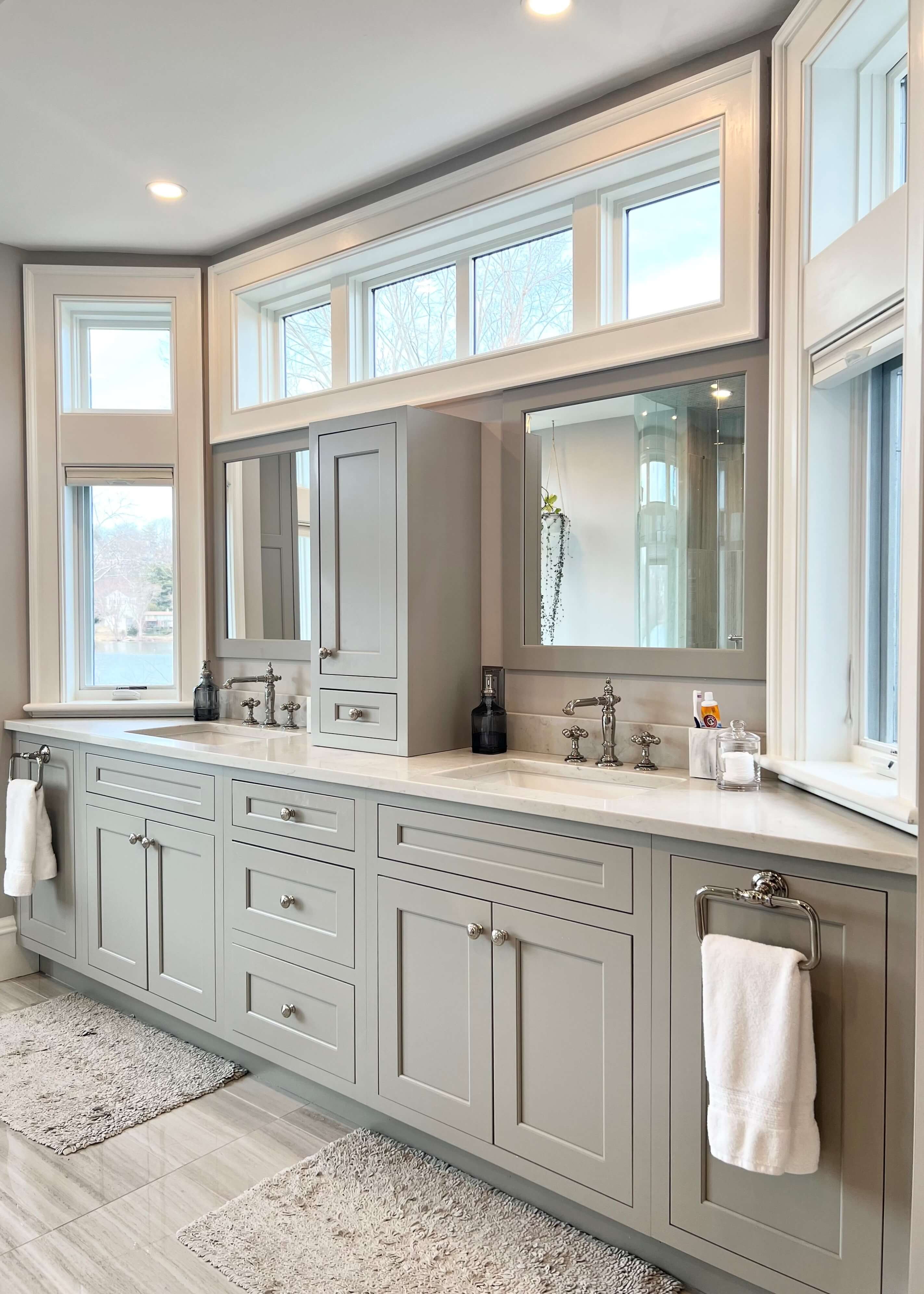 Custom bathroom vanity cabinets in a soft light gray painted finish create a serene, spa-inspired retreat. A long double-sink vanity, abundant drawer storage, and polished chrome cabinet hardware combine timeless style with everyday functionality.