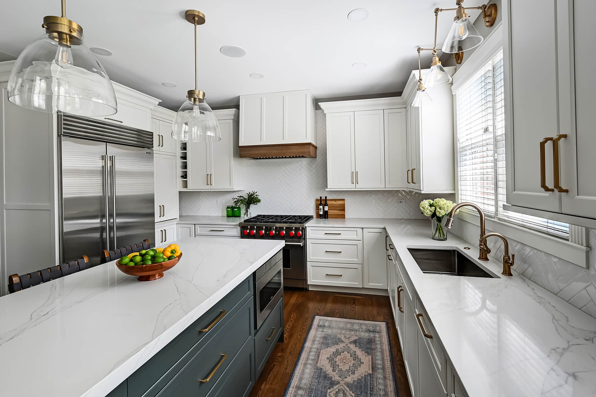 Two-tone custom kitchen cabinets pair bright white painted perimeter cabinetry with a dark painted kitchen island for timeless contrast. Warm brass cabinet hardware and plumbing fixtures add elegance, while a large island creates a welcoming hub for cooking and gathering.