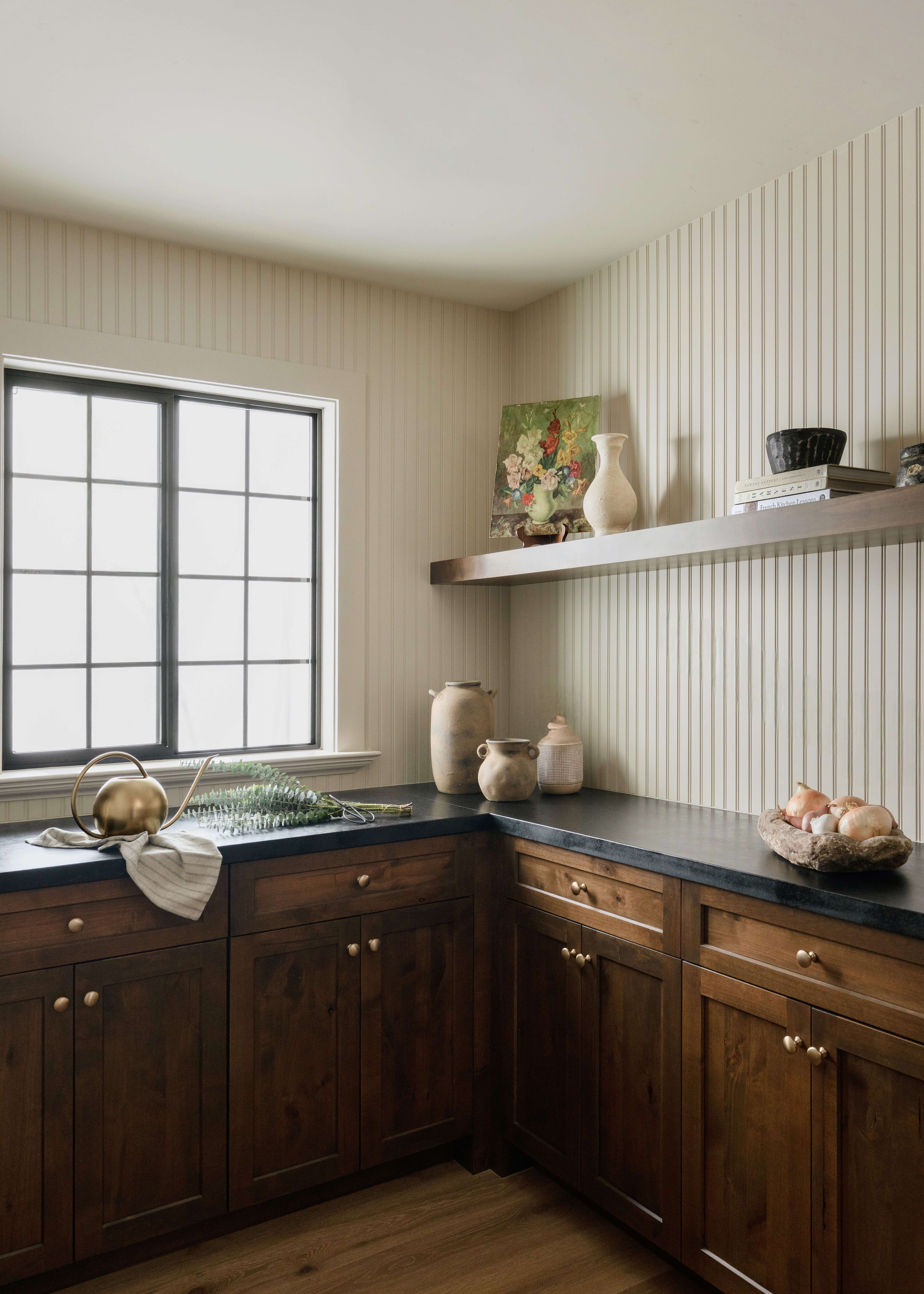 Butler's pantry cabinets showcase a rich true-brown stained finish paired with dark countertops and floating wood shelves. Thoughtful storage, vertical wall paneling, and warm wood tones create an inviting space for serving, storage, and entertaining.