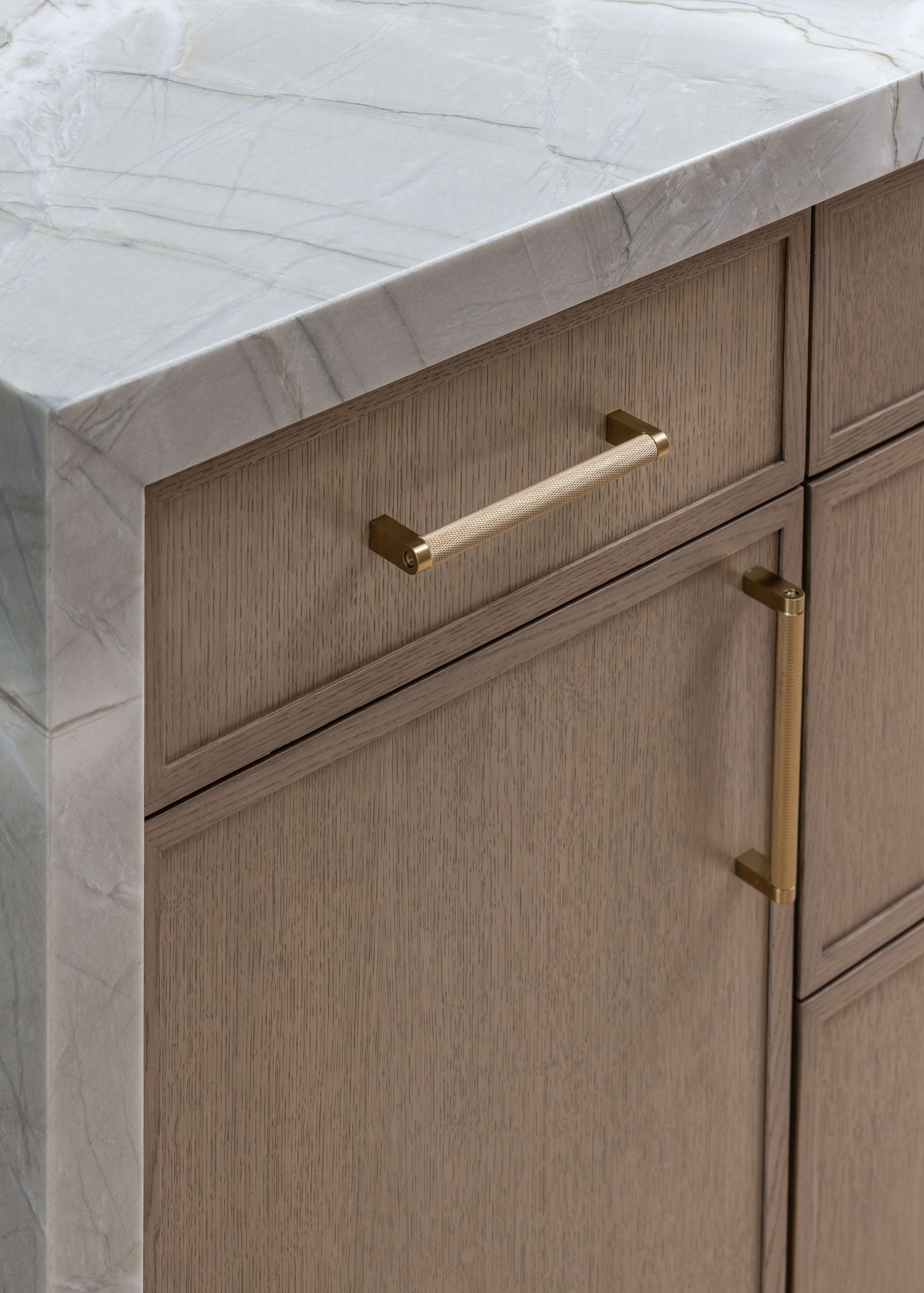 Slim shaker custom kitchen cabinets in a true-brown stain showcase natural wood grain and modern brushed brass hardware pulls. This warm, contemporary cabinetry design pairs clean lines with elevated finishes for a timeless and sophisticated kitchen aesthetic.