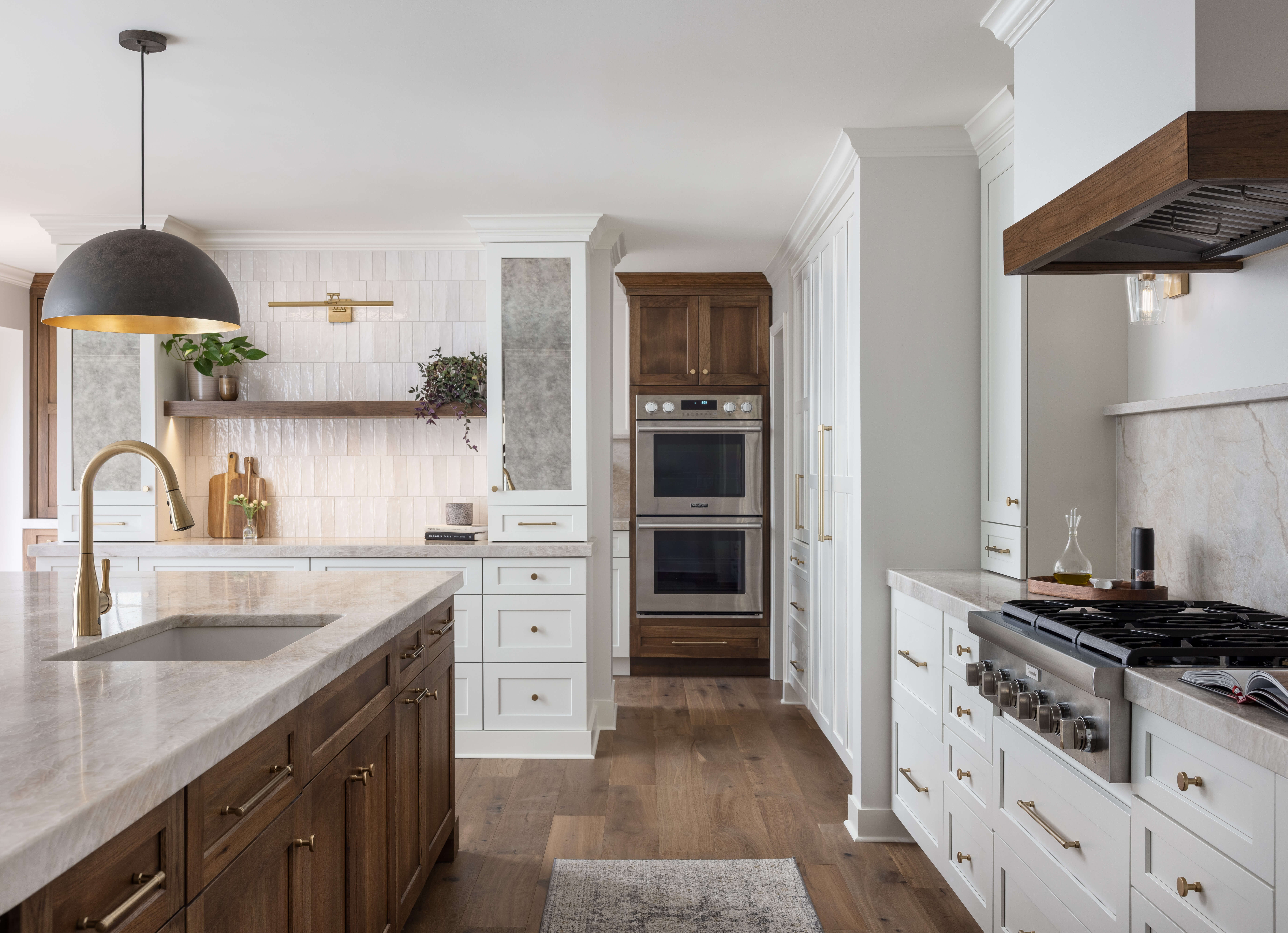 These two-tone custom kitchen cabinets blend warm stained wood cabinetry with bright white painted cabinets for a timeless, inviting design. Elegant brass cabinet hardware adds warmth and sophistication, while the contrasting finishes create depth and visual interest throughout the space.